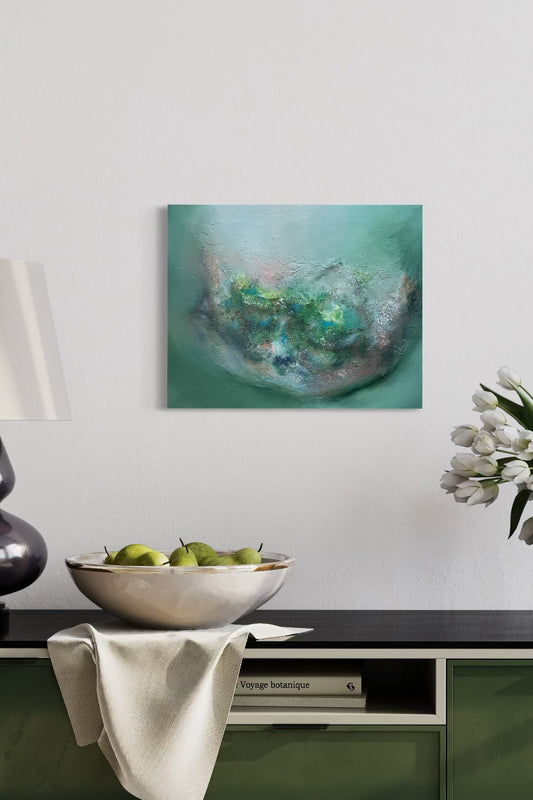 Abstract painting on a wall above a table with a bowl of apples and a lamp.